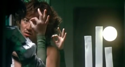 A close-up screenshot of a man and a female android both holding an ok sign to each other from the movie '2046'.