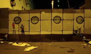 [Captured at night, this photo shows a mural fashioned as the hull of a boat. The artists’ discarded stencil papers lie nearby.]