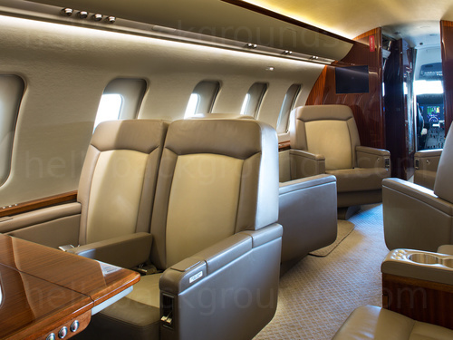 Private jet interior with angled view of cream leather seats and view of the aircraft cockpit Zoom background