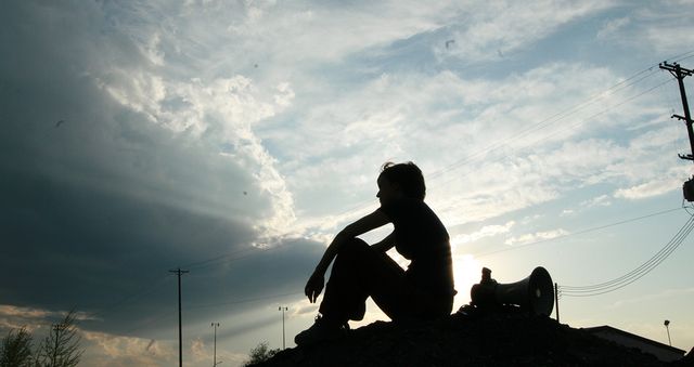 Silhouette sitting on a hill, beside a bullhorn