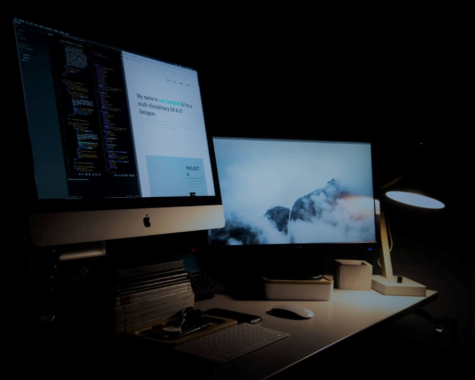 Two computer screens on a desk showcasing code and a website of a UX and UI designer.
