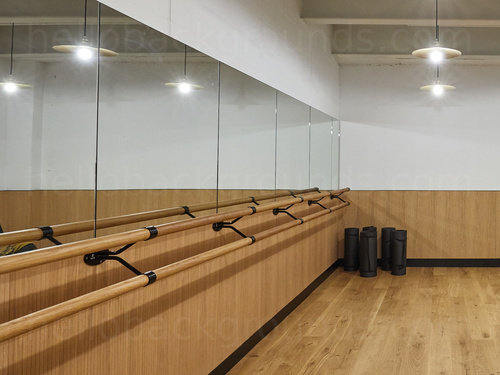 Exercise and yoga studio with wooden floor and large mirrors on one wall, and hand bar with rolled up yoga mats Google Meet background