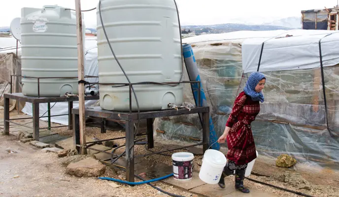A Syrian refugee woman carries two buckets full of water