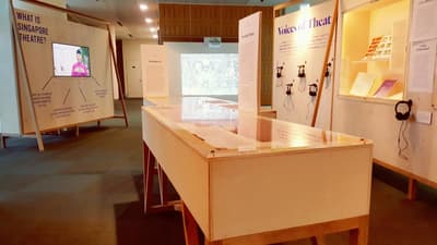A table showcase is in the middle. On the left, there is a wall with a TV screen, showing a video. On the right wall, there is a wall showcase and several headphones for playing sound samples.