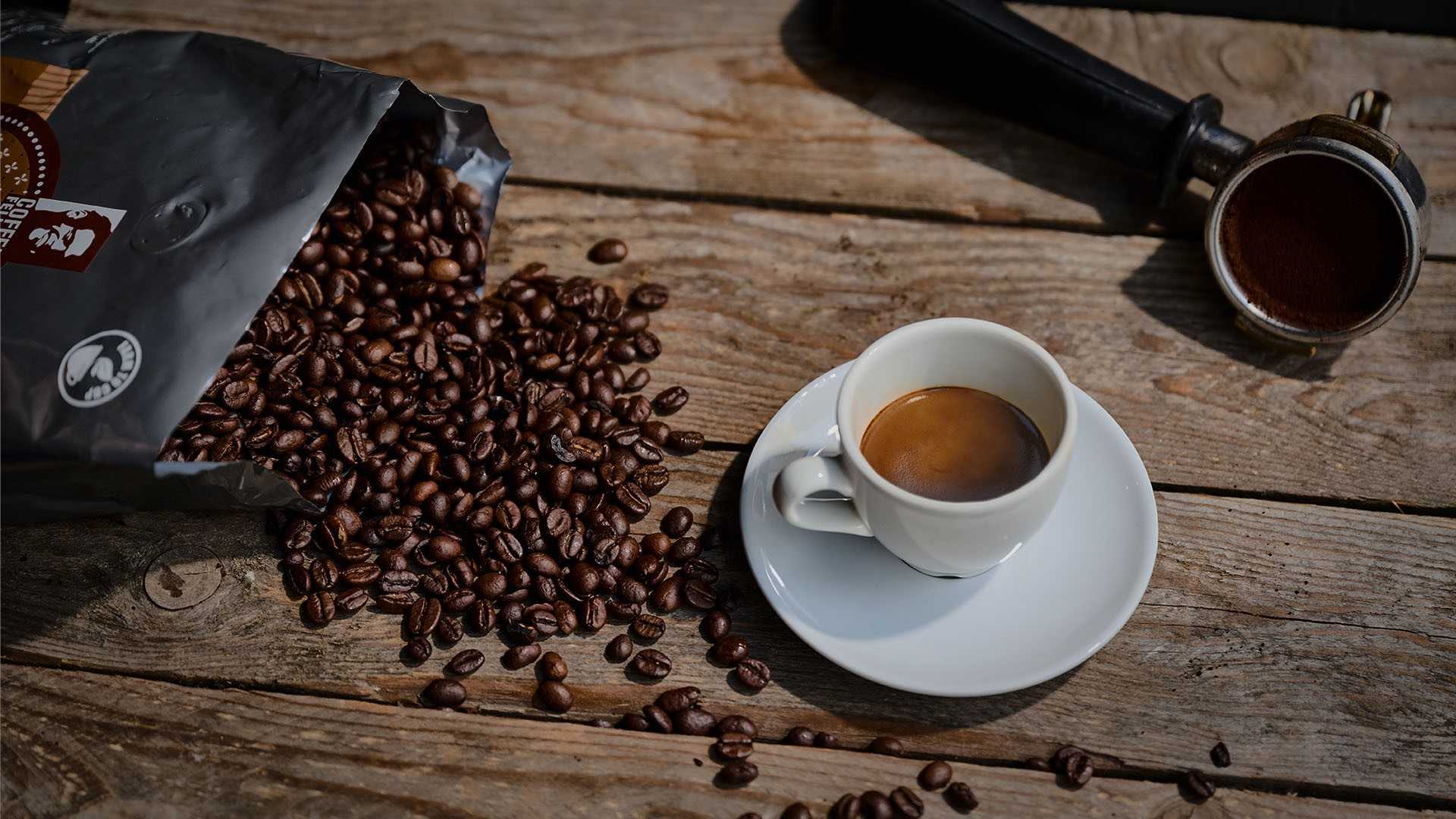 Gefüllte Espresso Tasse, geöffntete Tüte mit Kaffeebohnen die aus der Tüte geschüttet wurden