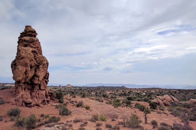 A lone pillar of red sandstone emerges from the desert ground in Arches National Park.