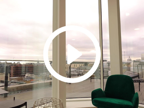 Green chair in front of large windows looking out to modern roof terrace with wooden decking and city skyline views Google Meet background