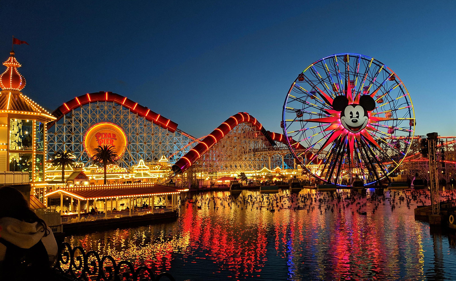 color photo of pixar pier at night with ferris wheel lit up in color showing the face of mickey mouse