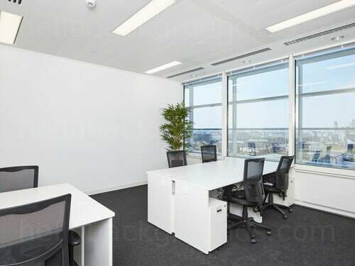Simple shared workspace featuring white desks with black office chairs next to potted plant and windows with city view Google Meet background