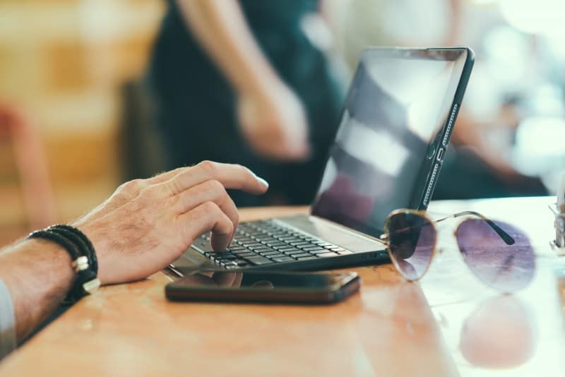 man working on computer with mobile phone and sunglasses on table