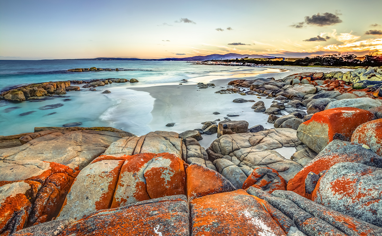 dramatic orange and gray rocks at the edge of the bay of fires in tasmania