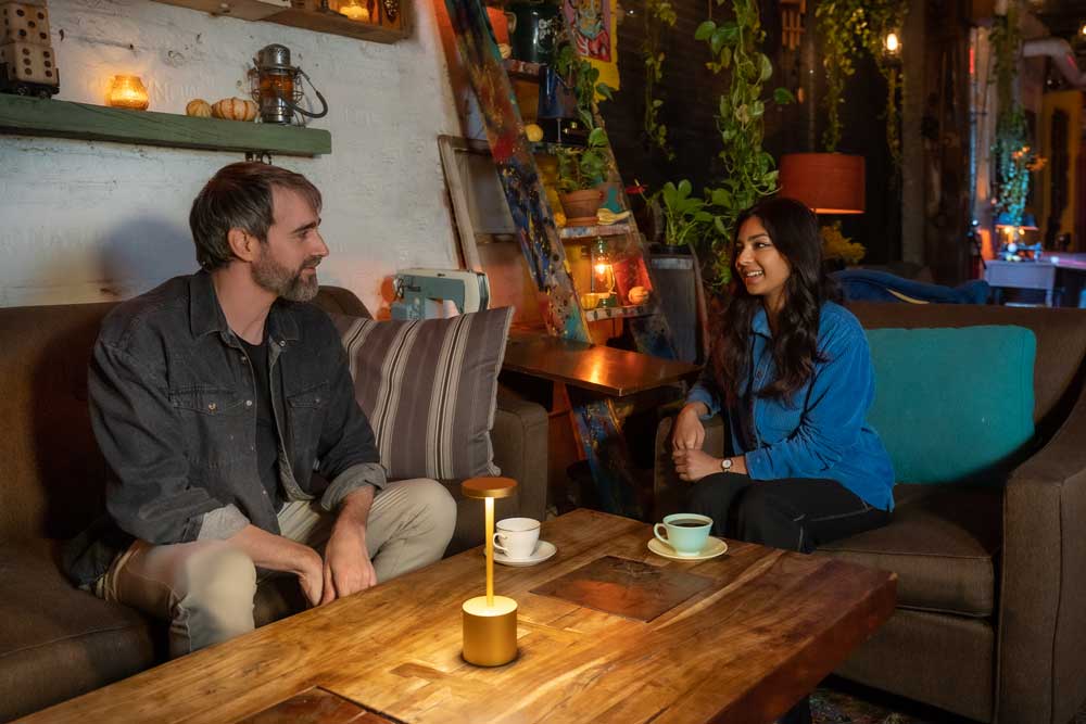 Photo of a man and a woman in conversation while sitting at a low coffee table in an intimately-lit indoor space.