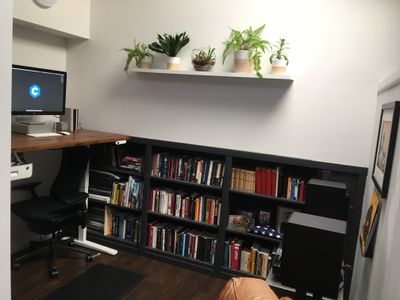 An office with a bookshelf, regular shelf, desk and monitor