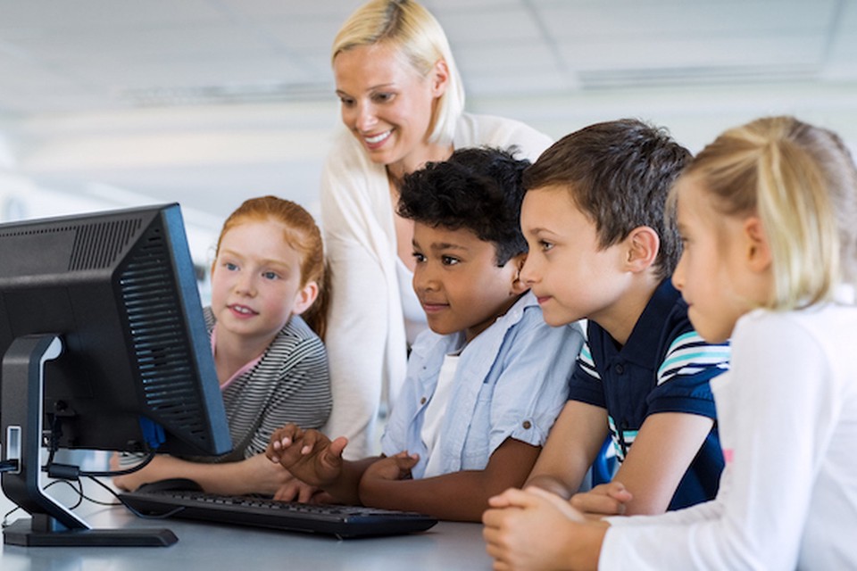 A female teacher shows her students something on a computer