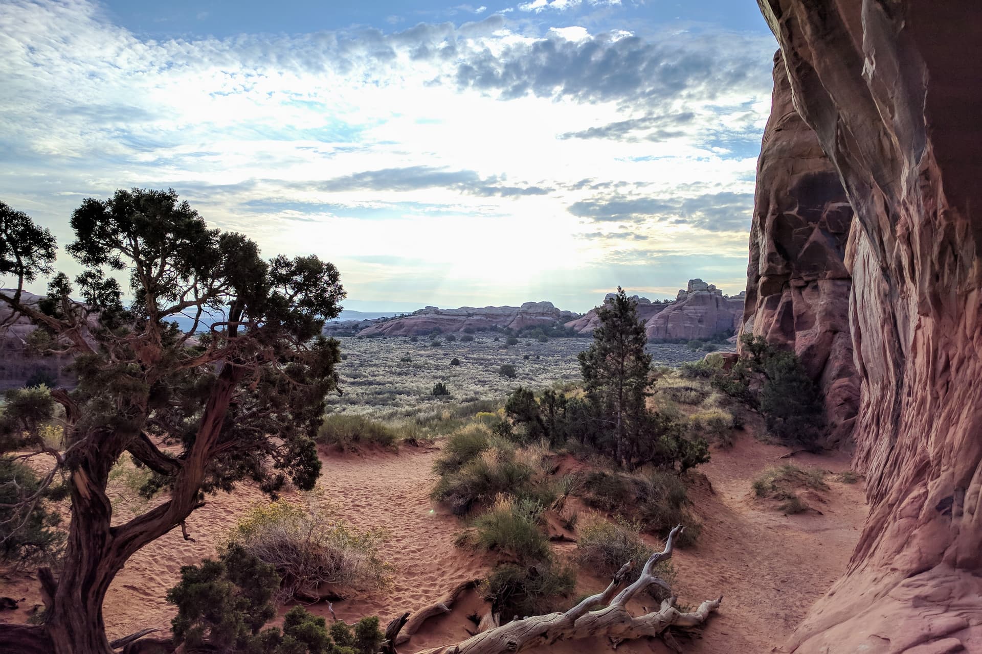 An oblique view through Pine Tree Arch in Arches National Park towards the rising sun. Unusually shaped sandstone mounds and pillars can be seen in the distance.