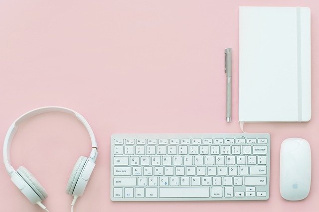 headphones, keyboard and mouse laid out on a pink background