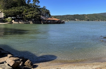 Vista da água com montanhas ao fundo e restaurante com mesas em deck sobre a água.