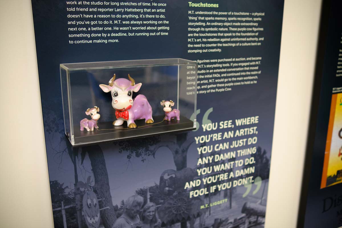 Panel-mounted artifact case with three purple cow figurines