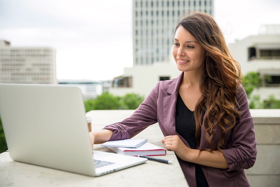 A woman smiling at a laptop screen while she types something