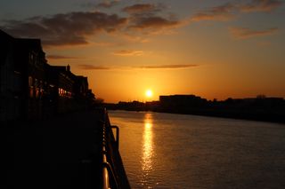 Sun setting behind the rooftops of Shoreham town. The sun is reflecting onto the river Adur below and the silver railings that line the river.
