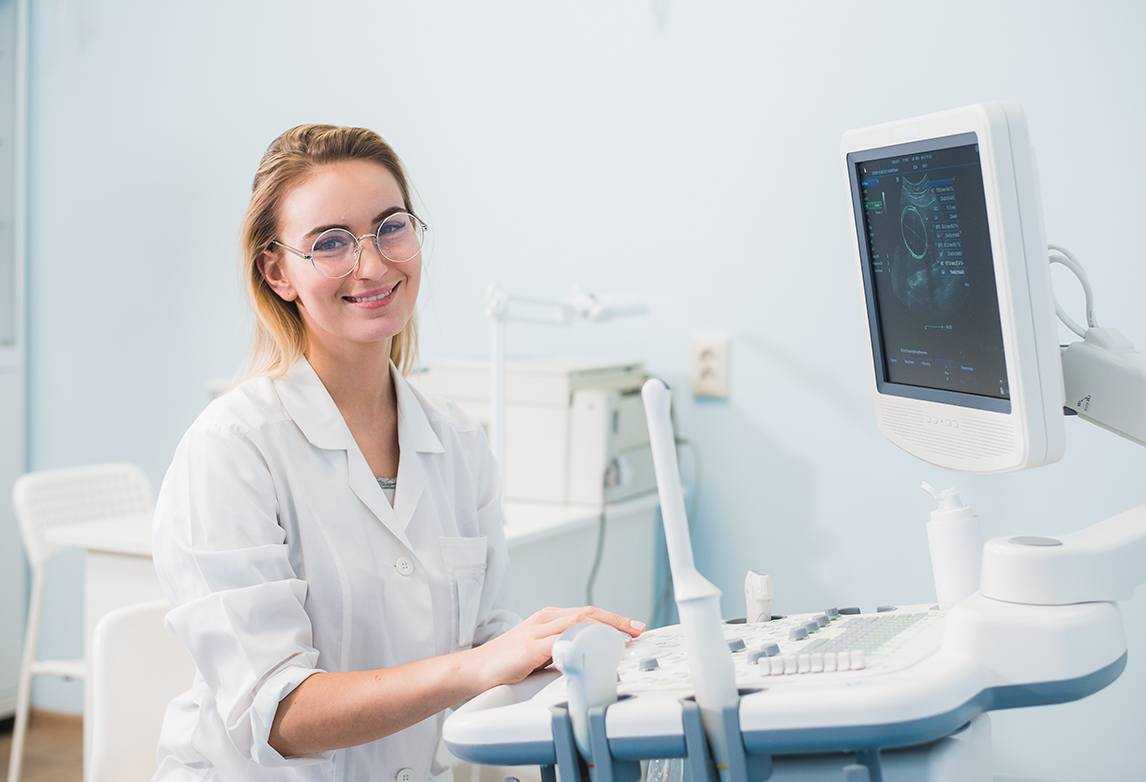 A healthcare professional smiles while looking at a sonogram machine.