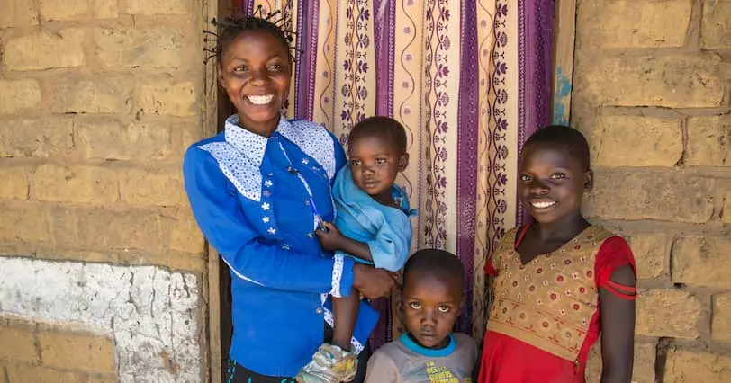 Joelle Inamulongo stands in the doorway of her home in DRC with her 3 children