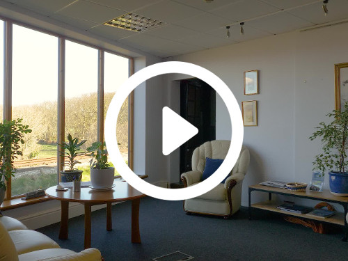 Airy private office with large windows presenting natural forest views containing cream furniture and round wooden table   Skype background