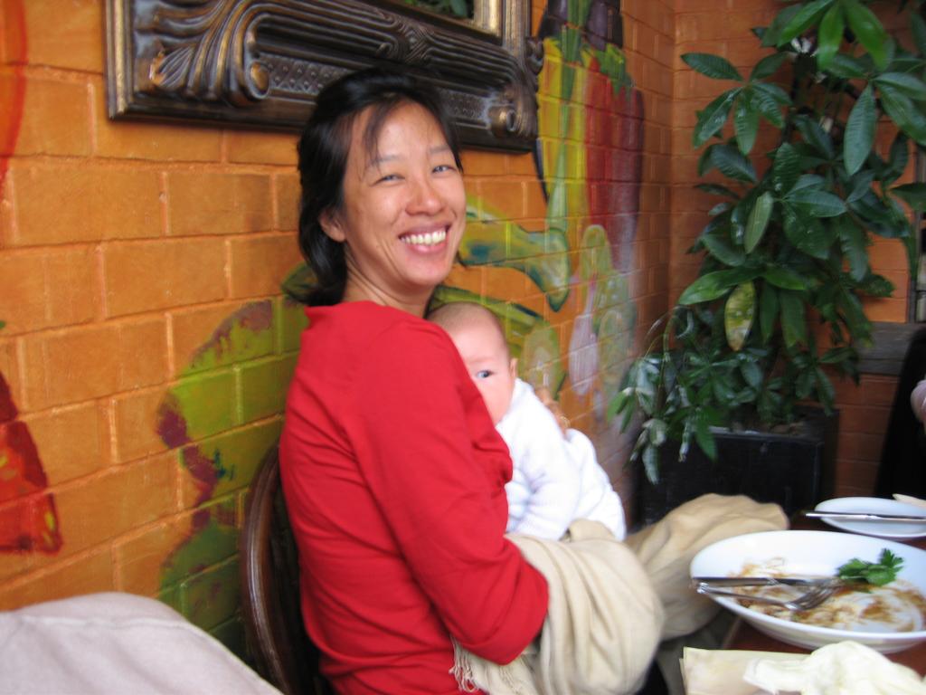 A Singaporean woman looks into the camera smiling, whilst holding a small baby