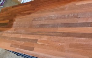 A Jarrah wooden desk top that is partially oiled, the oiled portion is a much richer and darker colour than the bare wood