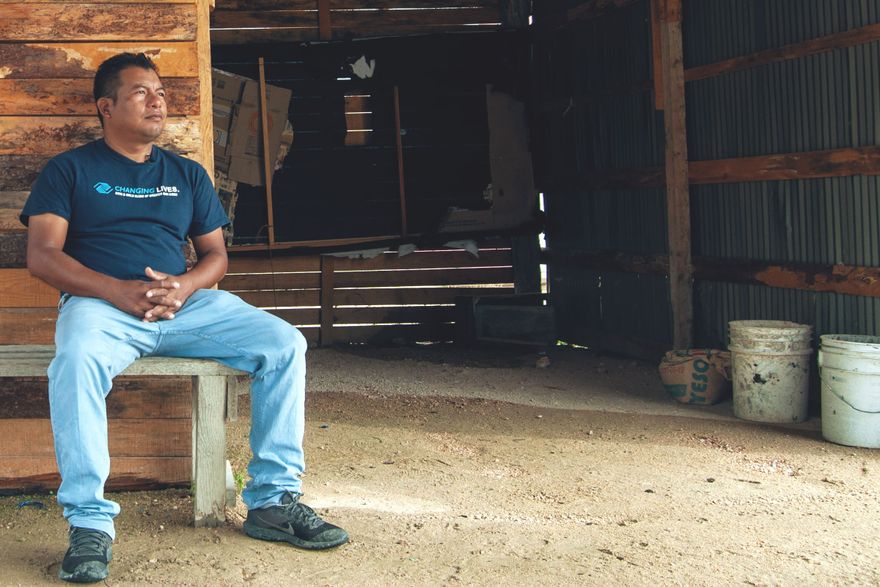 enoc, wearing jeans and a t-shirt, sits on a wooden bench in his garage