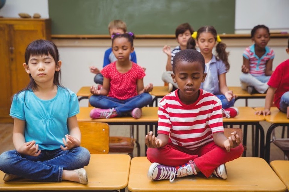 Students sit on desks while meditating.