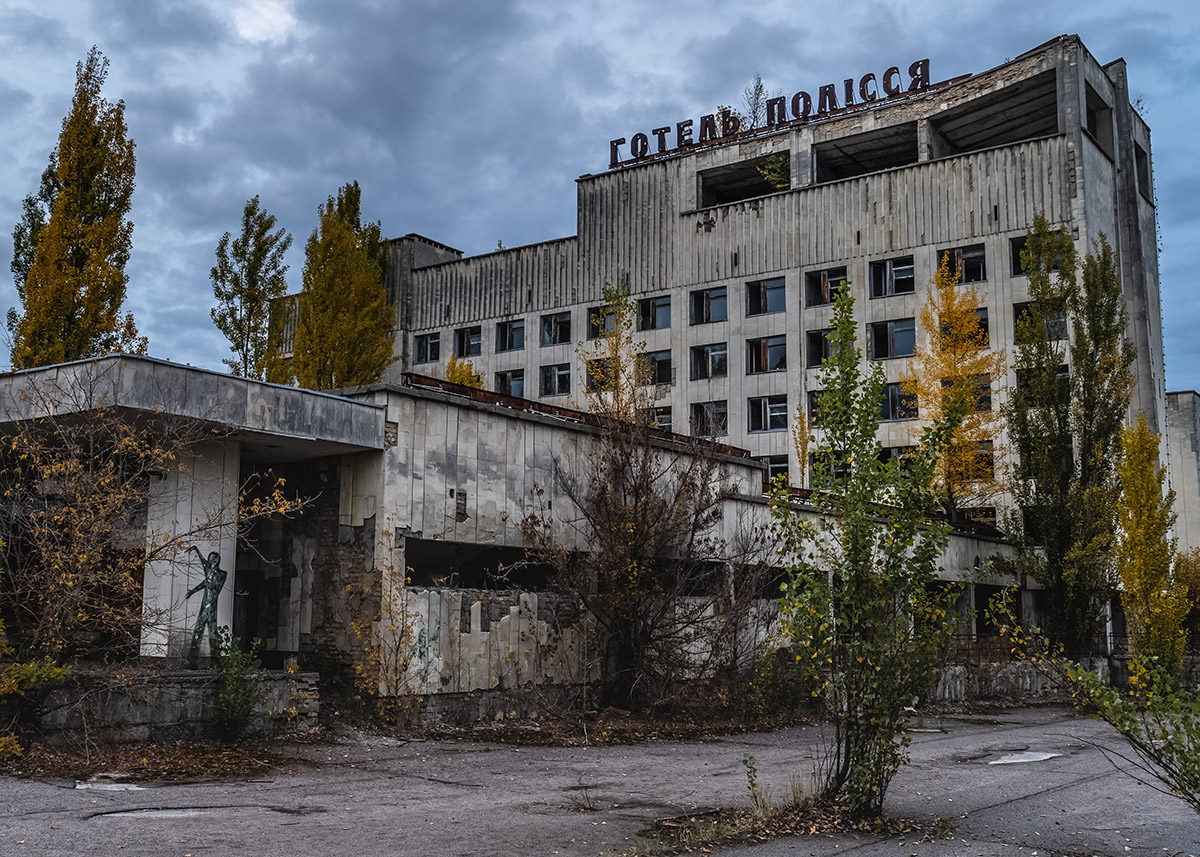 dilapidated concrete building with scraggly plants and a sign on top in russian letters in chernobyl, ukraine