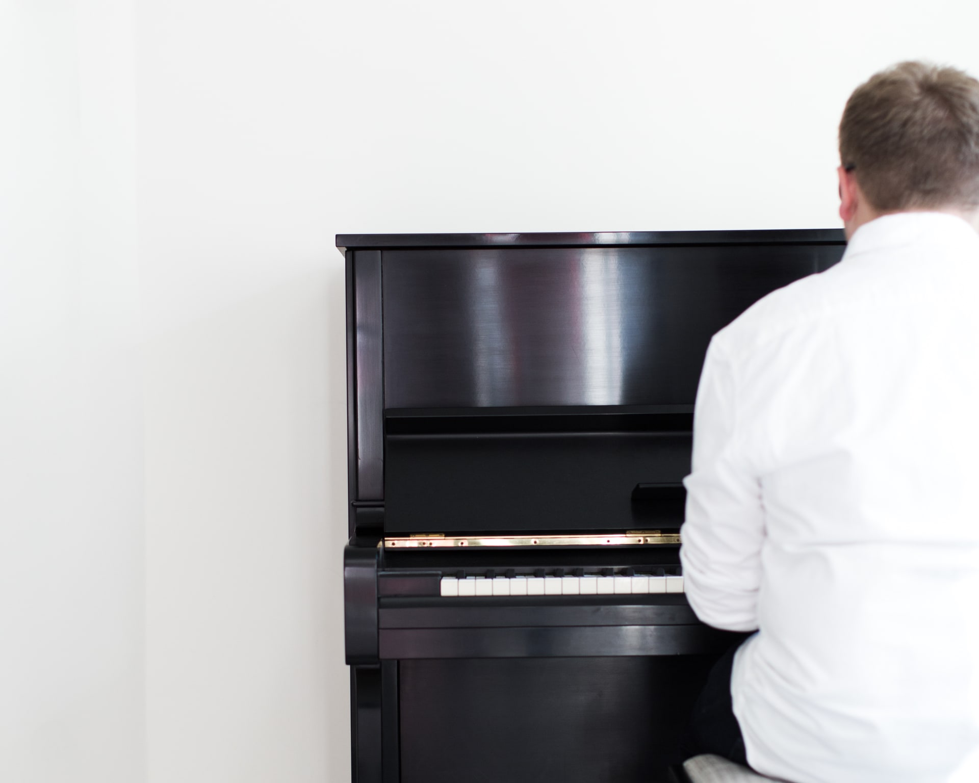 Jack Watkins playing a black Yamaha upright piano in a simple, light filled white space