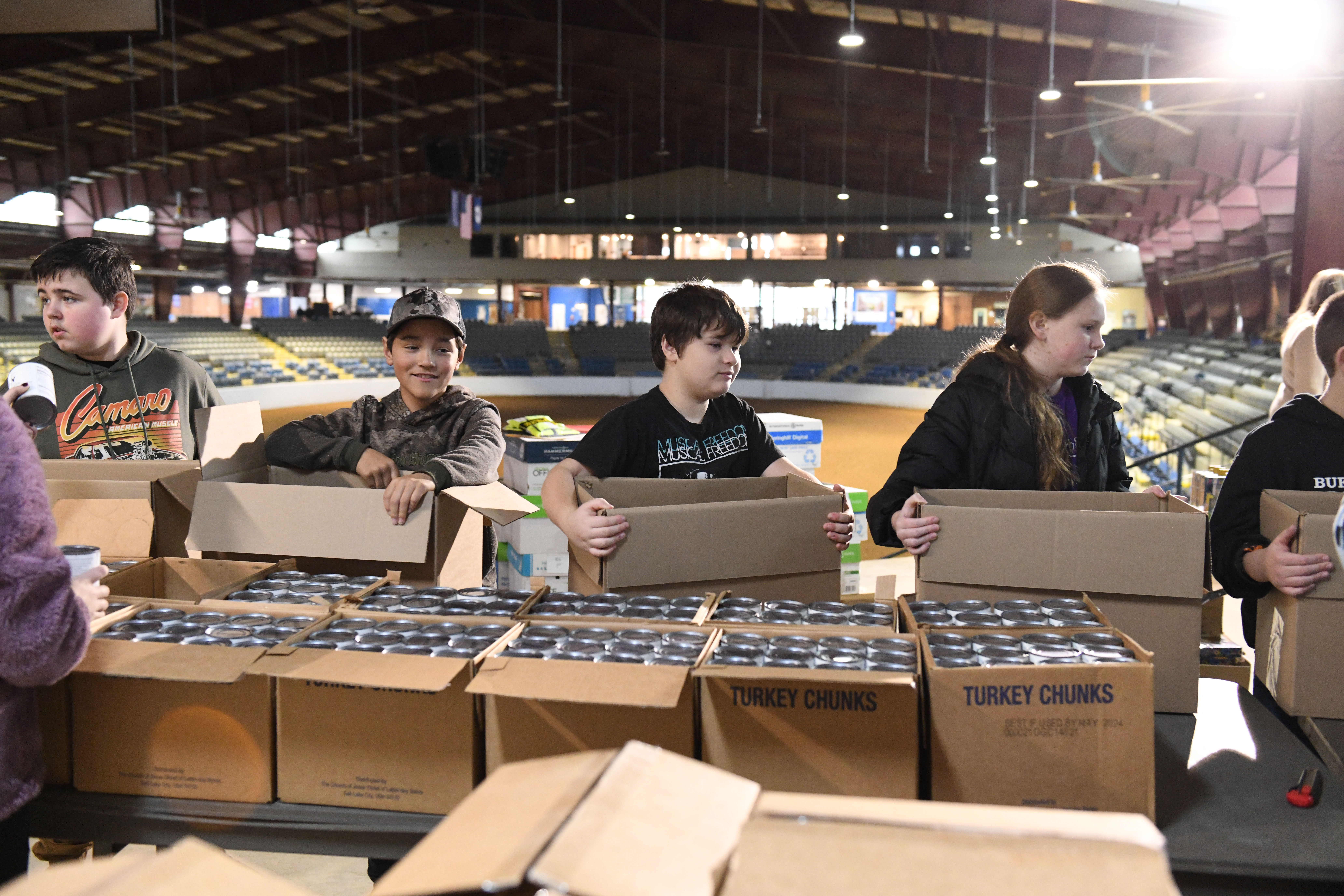Three boys and one girl in line, each with a large cardboard boxes in hand, ready to add canned goods.
