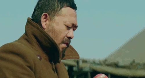 An animated gif of a scene from the film 'A Touch of Sin' of a middle-aged man, Dahai, as he blows dirt of an orange. Suddenly there's an explosion behind that startles him.