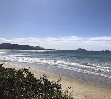 Vista do mar da barra da lagoa com faixa de area e logo atrás o mar com céu azul e raios de sol