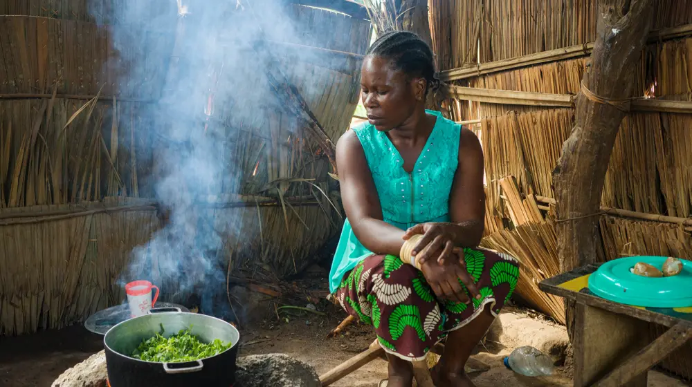 A Central African woman prepares a meal of amaranth leaves, peanut paste and plantain after a cooking demonstration with her neighbor