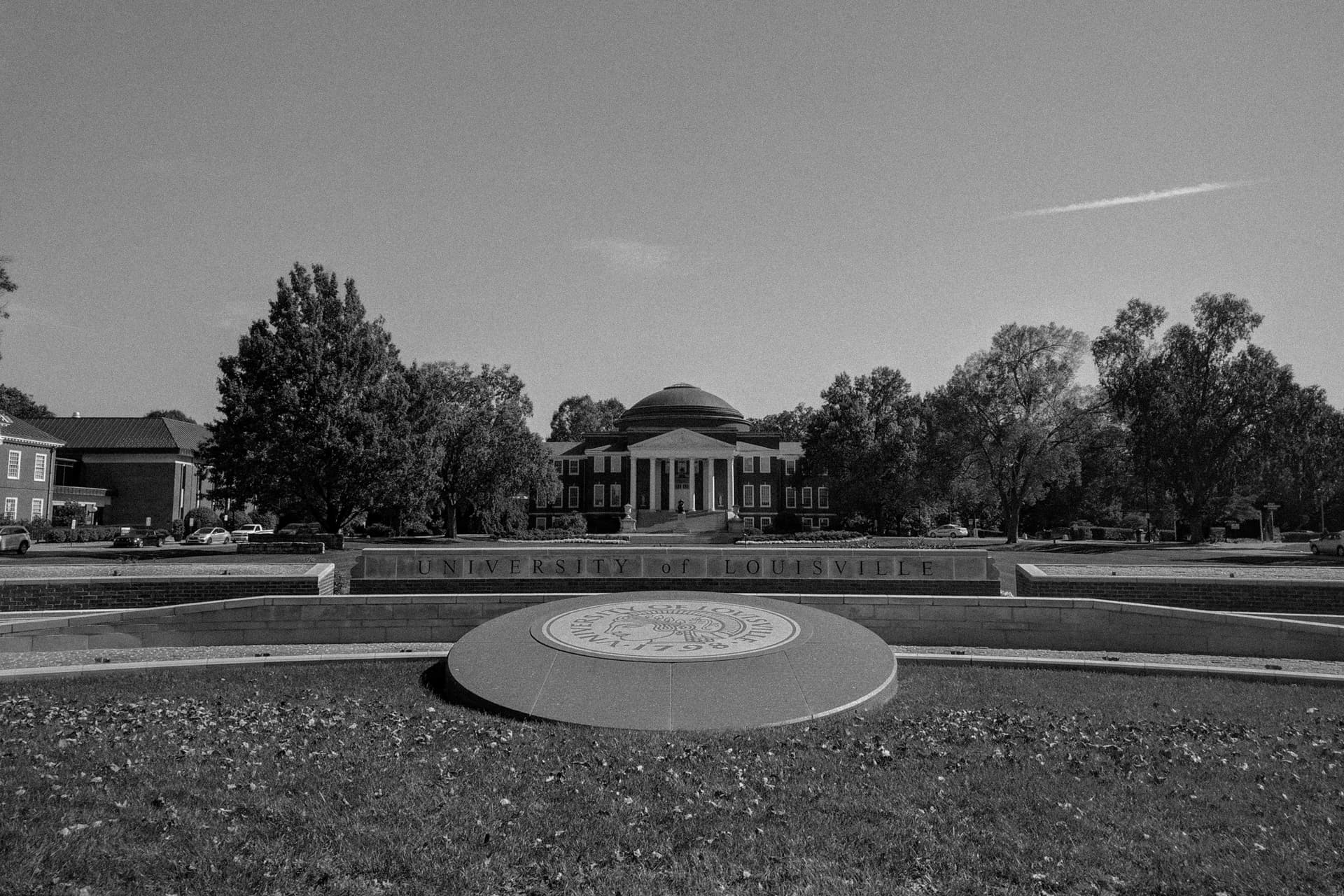 A prominent domed building on the campus of the University of Louisville. In the foreground is a stone carved into an image of the university's seal.