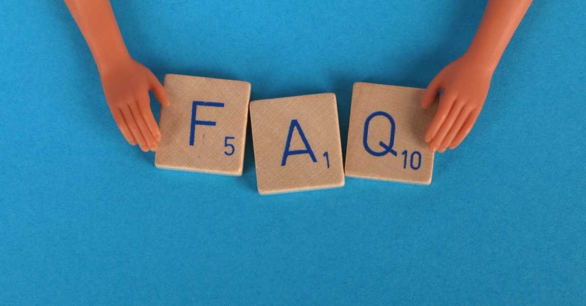 Zwei Hände halten die Buchstaben F, A und Q auf Scrabble-Steinen vor einen blaunen Hintergrund