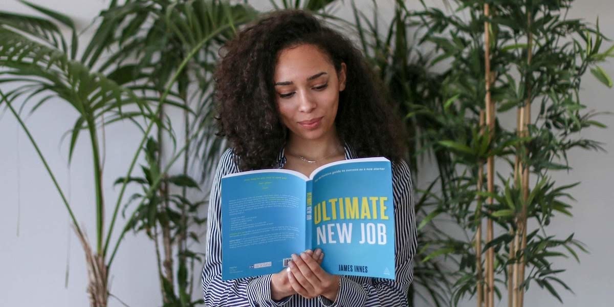 Get started in UX design with the help of these 11 great books A woman UX designer reading a UX design book in front of a plant in an office