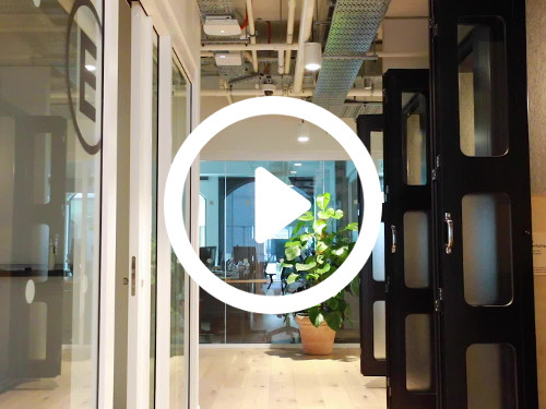 Modern style workspace with exposed ceiling above multiple black sliding doors opposite white framed office entrance Zoom background