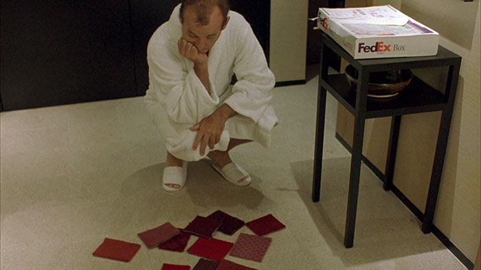 Scene from the movie Lost in translation where Bill Murray is looking at multiple colored cloth tiles in the ground.