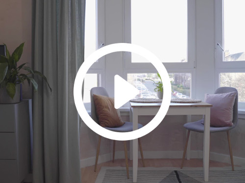Home dining room interior featuring large windows with sub-urban views behind small white table with purple chairs Zoom background