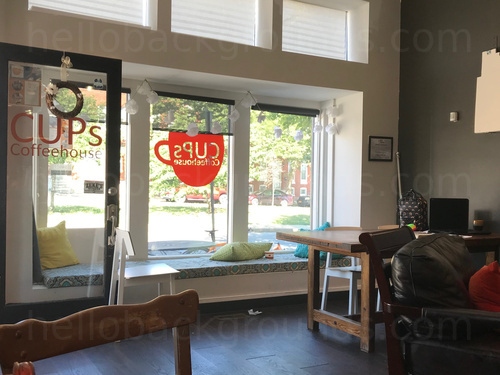 Simple cafe interior with wooden tables and chairs as well as padded arm chairs featuring street views  Microsoft Teams background