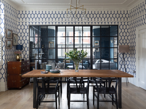 Modern style dining room featuring large interior window with living room beyond and wooden dining table with black chairs  Skype background