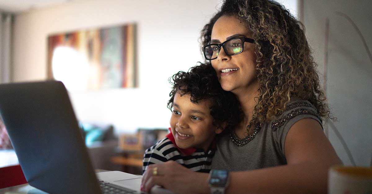 A woman holds her son while using the computer. Learn more about how GROW is using technology to give back.
