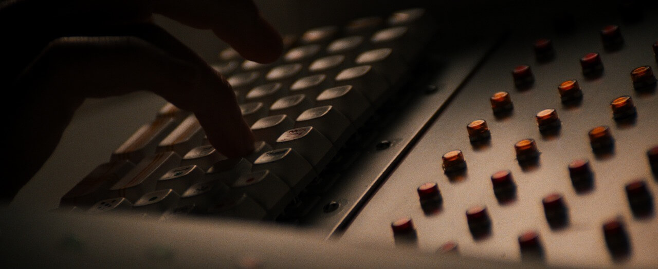 Image showing a close up of a hand in shadow typing on a retro-futuristic keyboard with thick key caps, a scene from the movie Alien.