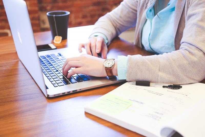 woman sitting at table and using laptop with tea cup in background