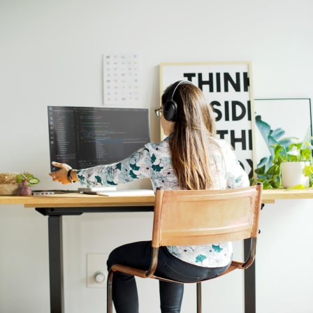 Girl sitting at a desk with headphones adjusts here montior.