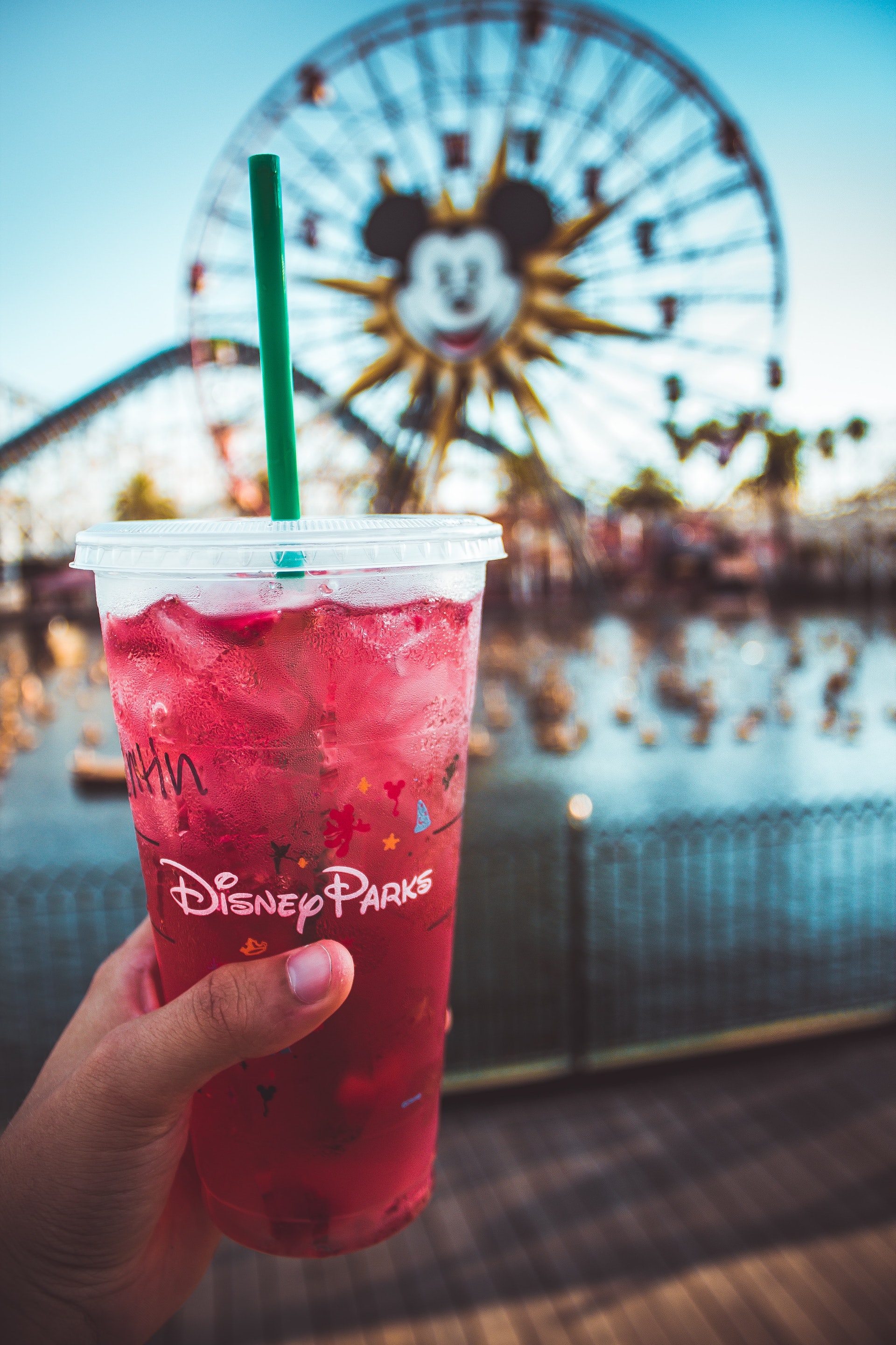 Someone holding up a cold drink in a Disney plastic cup in Disneyland.